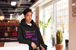 Woman wearing black pull over hoodies with the word "You Are Enough said God" in pink and purple text
