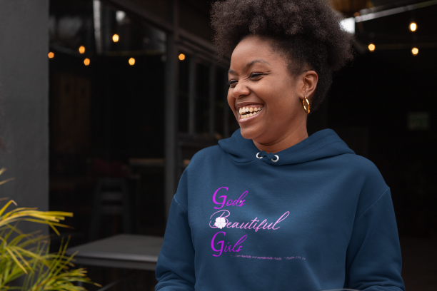 African American woman with Afro puff wearing a navy pull over hoodie with the words "God's Beautiful Girls" in purple and pink letters on the front. 
