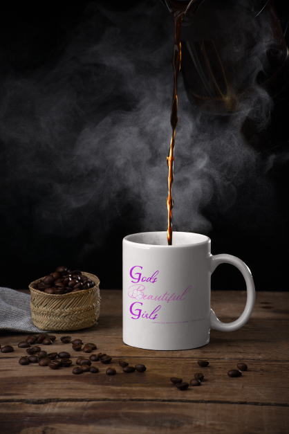 Coffee being poured into a white ceramic God's Beautiful Girls mug with purple and pink letters on the front. Steam is rising form the mug and coffee beans are to the left of the mug.